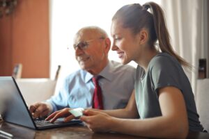 Elderly man sitting at a computer with young woman.